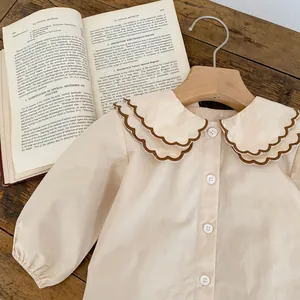 Detail eines vintage beigen Babyhemds aus Baumwolle mit doppeltem Wellenkragen und Knöpfen
