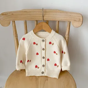 Close-up of baby knit cardigan with mushroom embroidery and wooden buttons on cream fabric