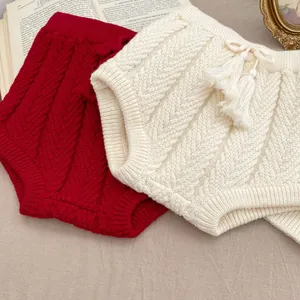 Detail von Strick-Babyshorts mit Quasten und Kordelzug auf rustikalem Stoffhintergrund