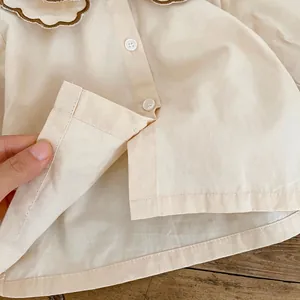 Detail der Babybluse mit brauner Wellenstickerei und Knöpfen auf beige Baumwolle