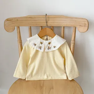 Détail du col Claudine blanc avec broderie florale sur un t-shirt côtelé jaune pour bébé