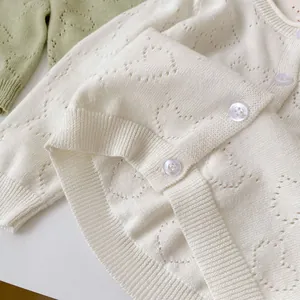 Detailed view of heart-shaped hollow knit pattern and buttons on white baby cardigan