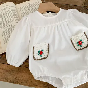 Detail of white long sleeve baby romper featuring delicate floral crochet pockets
