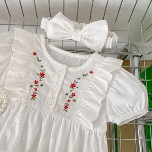 Infant white cotton bodysuit set with floral embroidery and bow headband on metal mesh