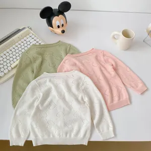 Flat lay of knit baby sweaters with heart cutouts in green, pink and off-white colors