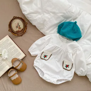 Flat lay of a white long-sleeve baby romper with floral pockets and knit hat