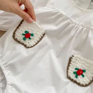 White cotton baby bodysuit featuring handmade crochet pockets with red floral embroidery