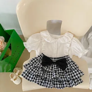 Close-up of baby girl white ruffled shirt and plaid tiered skirt with a black bow