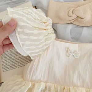 Détail de robe bébé fille avec nœud en perles, manches en tulle à pois et bandeau