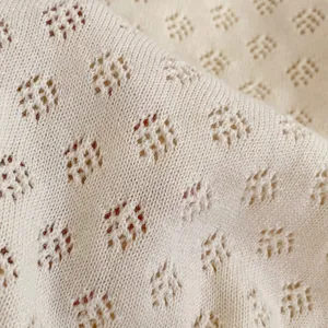 Close-up of cream knit baby romper featuring delicate diamond hollow patterns and soft texture
