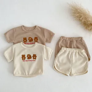 Flat lay of baby waffle knit sets with bear embroidery in cream and light brown colors