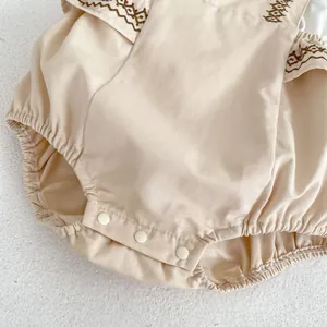 Detail of baby romper featuring scalloped embroidery edges and three white snap buttons