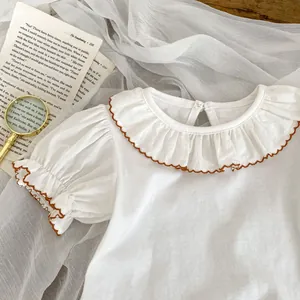 Detail of white cotton baby blouse with ruffle collar and brown wave stitched edges