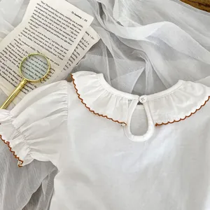 Detail of baby girl white top featuring ruffle collar with brown embroidery edge