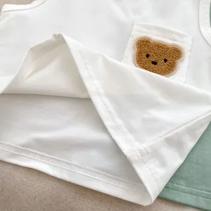 Close-up of white baby cotton tank top featuring a cute plush bear pocket detail