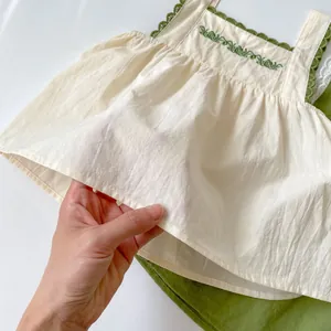 Detailed view of the green vine embroidery and ruffle trim on this white baby tank top