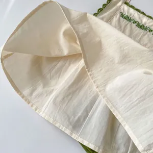 Detail of cream cotton fabric with green floral embroidery and lace trim on baby clothing