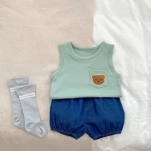 Flat lay of baby summer set with bear embroidery mint vest and denim shorts