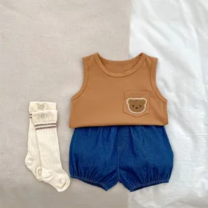 Flat lay of baby summer set with orange bear vest, denim shorts, and striped socks