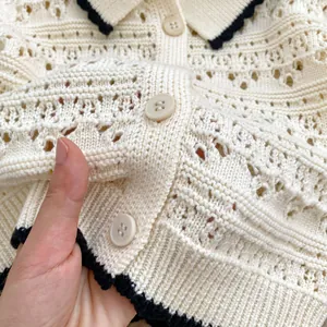 Close-up of cream knit cardigan featuring delicate hollow patterns and black crochet trim