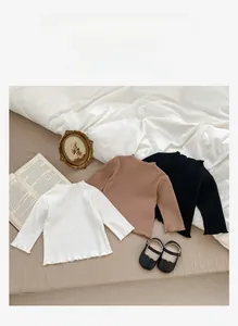 Detail of ribbed cotton baby shirts in white, brown, and black with ruffled edges