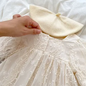 Dettaglio vestito in pizzo per neonata con ricami floreali e berretto in maglia abbinato