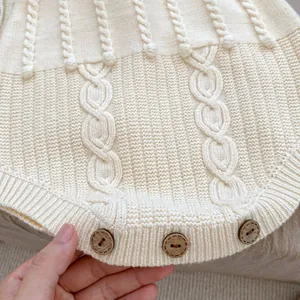 Detail of baby knit romper showing ivory cable pattern and three round wooden buttons