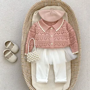 Flat lay of pink knit hollow cardigan, tutu jumpsuit, and beret in a woven basket