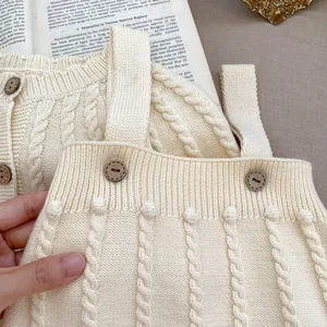 Detail of baby knit romper showing ivory cable stitch texture and wood buttons