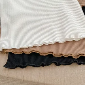 Detailed view of lettuce edge hems on ribbed cotton shirts in white, khaki, and black