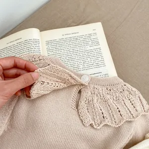 Knitted baby bodysuit in beige featuring a decorative hollow-out ruffle collar and button