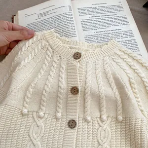 Detail of cream knit cardigan with cable stitch and decorative pom-poms and wood buttons