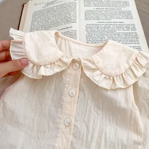 Détail d'une chemise bébé en coton crème avec col à volants et boutons blancs