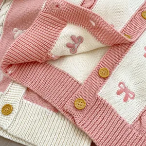 Detail of pink and beige striped knit cardigan with bow embroidery and yellow buttons