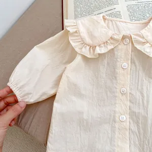Détail d'une chemise bébé fille beige avec col Claudine à volants et manches bouffantes