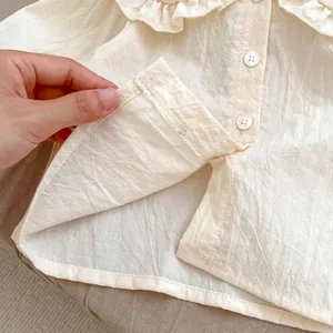Détail du chemisier bébé avec col à volants, texture crème et finitions de couture interne