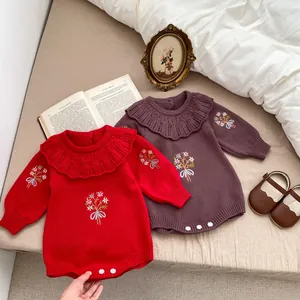 Detail of baby knitted rompers with ruffle collars and floral embroidery in red and purple