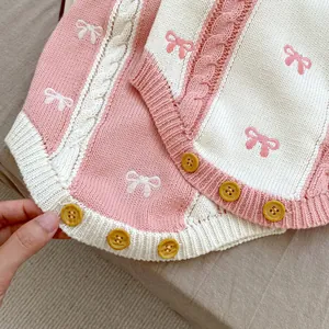 Detailed cable knit texture with pink bow embroidery and yellow buttons on baby cardigan
