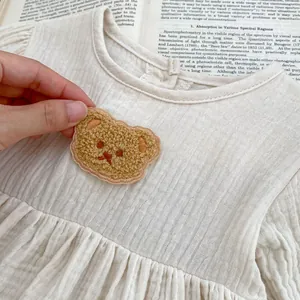 Detailaufnahme der braunen Teddybär-Plüschstickerei auf dem gerafften Baby-Strampler