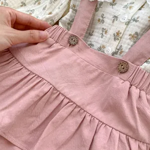 Close-up of floral shirt collar and pink corduroy suspender skirt with wooden buttons