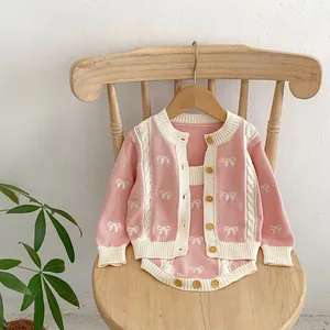 Detail of pink knitted baby cardigan with bow patterns and natural wood buttons