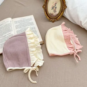 Detail of ribbed cotton baby bonnets with ruffle edges in purple and beige tones