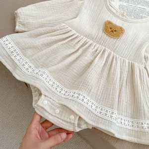 Detailansicht beige Baby-Einteiler mit Plüschbär-Patch und feiner Spitzenkante am Saum