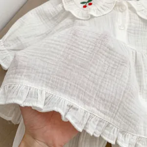 Détail du tissu en gaze de coton respirant blanc avec broderie cerise délicate
