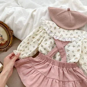 Detailed close-up of floral baby shirt with lace collar and pink suspender skirt