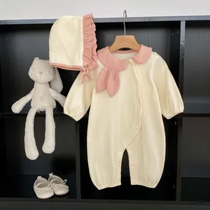 Detail of baby romper with pink Peter Pan collar and matching bonnet on a rustic shelf