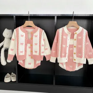 Infant girl knit set with pink bow cardigan and matching romper displayed on black wood