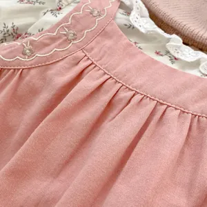 Dettaglio vestito neonata rosa in cotone con ricami floreali e scollo smerlato a onde