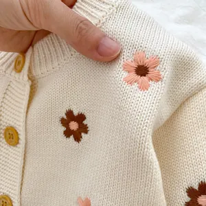 Détail d'un cardigan beige pour bébé avec broderies florales et boutons aspect bois