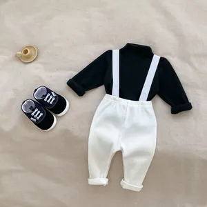 Flat lay of baby autumn outfit featuring a black long sleeve top and white ribbed trousers